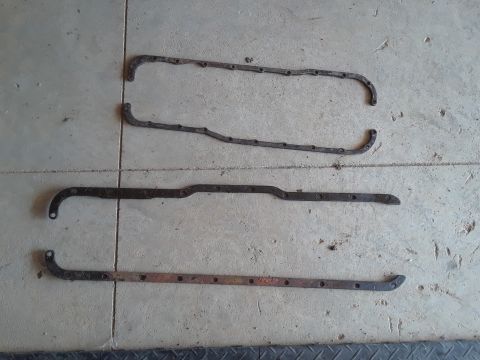1994 Ford Bronco - Three old, rusty metal gaskets are laid out on a concrete surface. The gaskets are of different shapes and sizes, with multiple bolt holes…