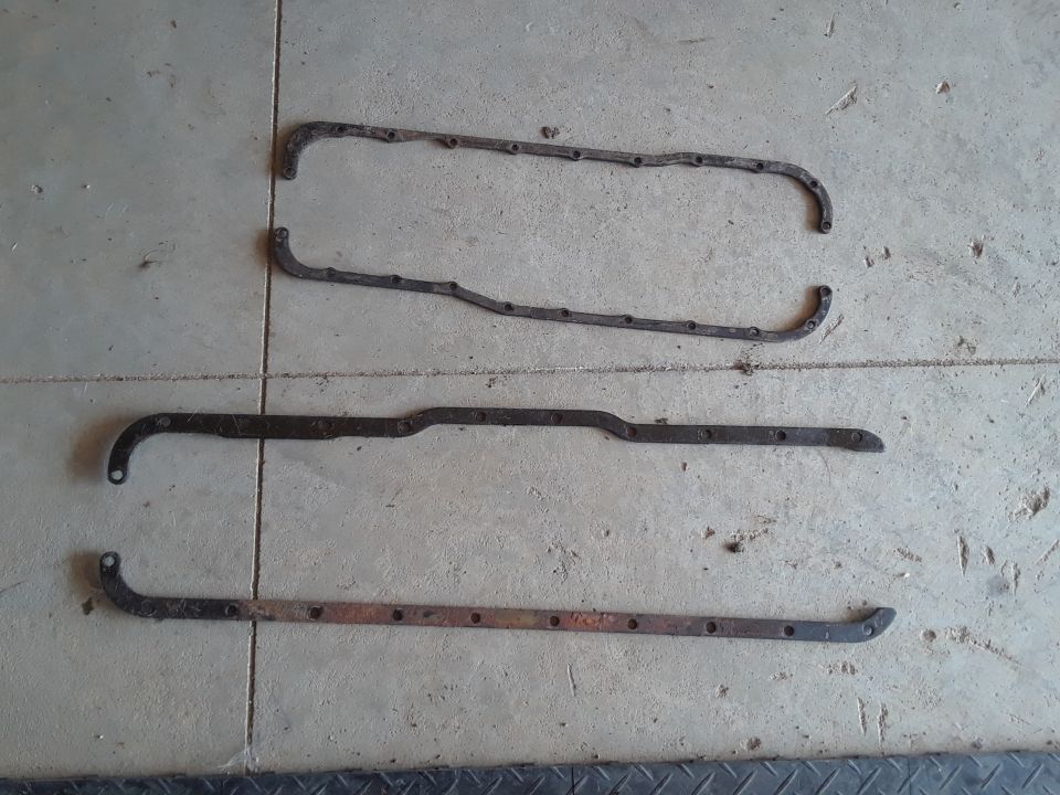 Three old, rusty metal gaskets with bolt holes on a concrete surface.