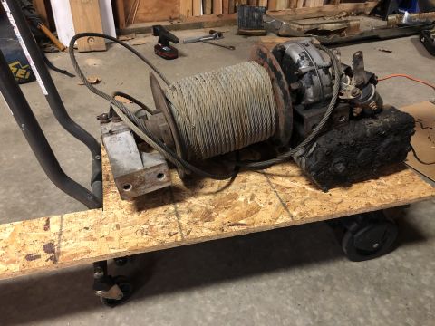 1980 Ford Bronco - A heavy-duty winch with a thick cable spool is mounted on a wooden platform with casters. The winch appears to be a mechanical or electric…