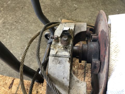 1980 Ford Bronco - A close-up view shows a rusty metal component with cables attached, possibly part of a winch or braking system, set against a concrete floo…