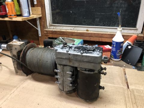1980 Ford Bronco - A heavy-duty winch with a thick cable spool is mounted on a concrete block. The winch appears to be a mechanical or electric model with a m…