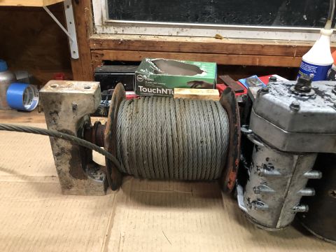 1980 Ford Bronco - A close-up view of a winch drum filled with cable, attached to a motor unit. Various tools and supplies are visible in the background.