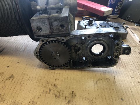 1980 Ford Bronco - A close-up view shows a disassembled winch gearbox with exposed gears and internal components. The scene is set on a cardboard surface, sug…