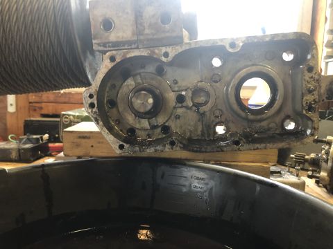 1980 Ford Bronco - A close-up view of a disassembled winch gearbox, showing internal gears and bearings covered in oil, resting above a black oil drain pan.