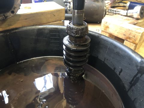 1980 Ford Bronco - A close-up view of a greasy, splined shaft partially submerged in dark fluid within a black drain pan. The shaft appears to be part of a me…