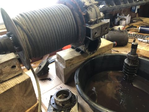 1980 Ford Bronco - A close-up view of a winch drum with a thick cable wound around it, resting on wooden blocks. In the foreground, a black oil drain pan hold…