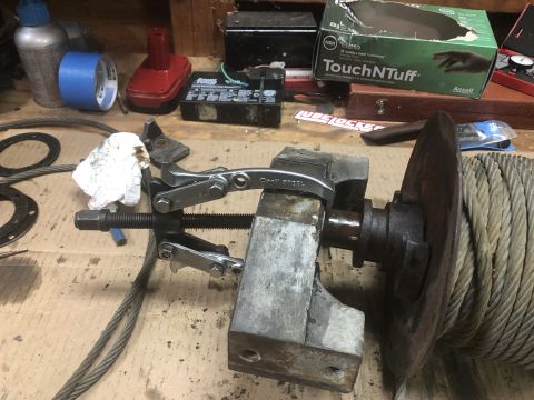 1980 Ford Bronco - A close-up view of a bearing puller tool attached to a metal shaft, with a large spool of wire rope to the right. Various tools and supplie…