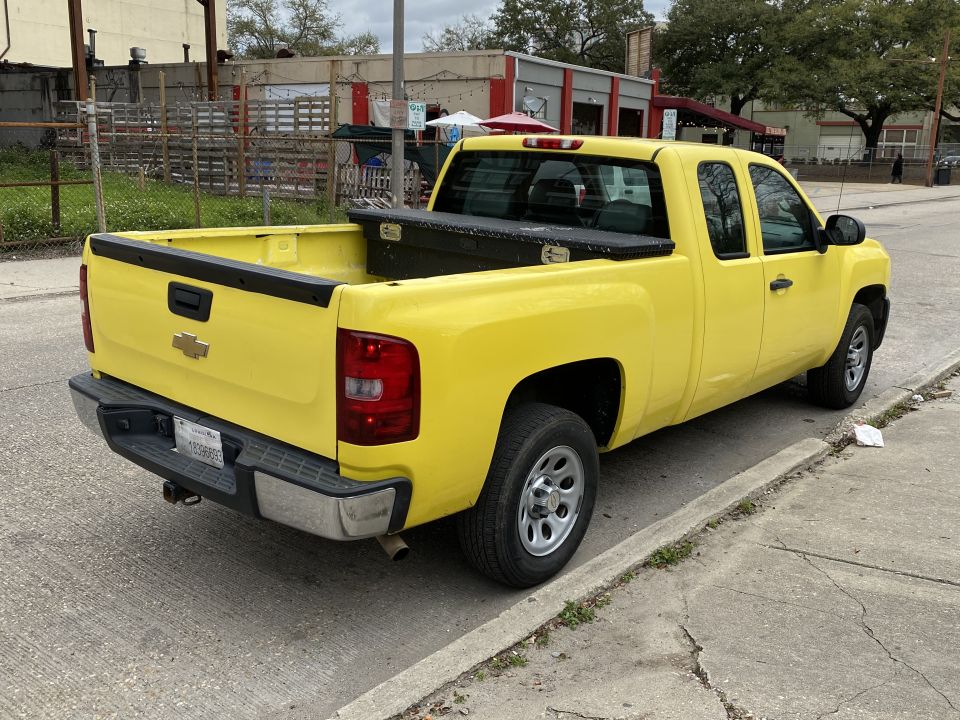 Yellow Chevrolet Silverado pickup truck parked on a street, rear passenger side view.