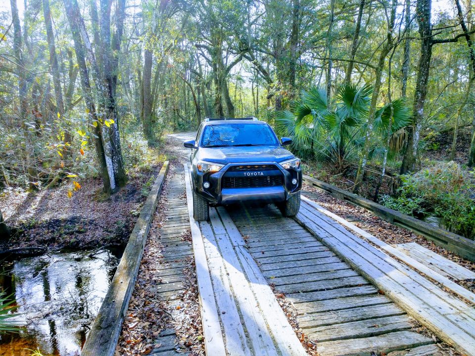 Black Toyota 4Runner on a wooden bridge in a forest.