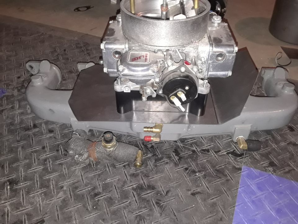 Custom gray intake manifold with carburetor on diamond plate surface.