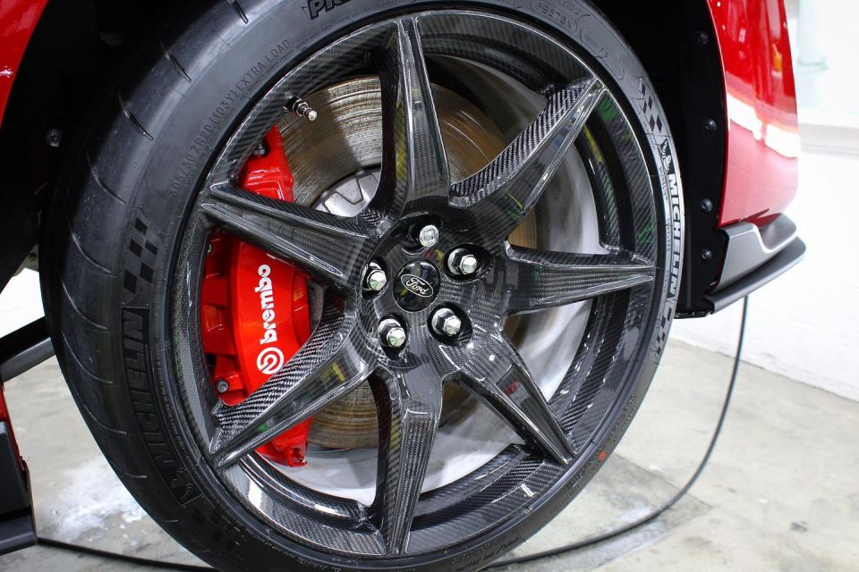 Carbon fiber wheel with red Brembo brake caliper on a red Ford Mustang.