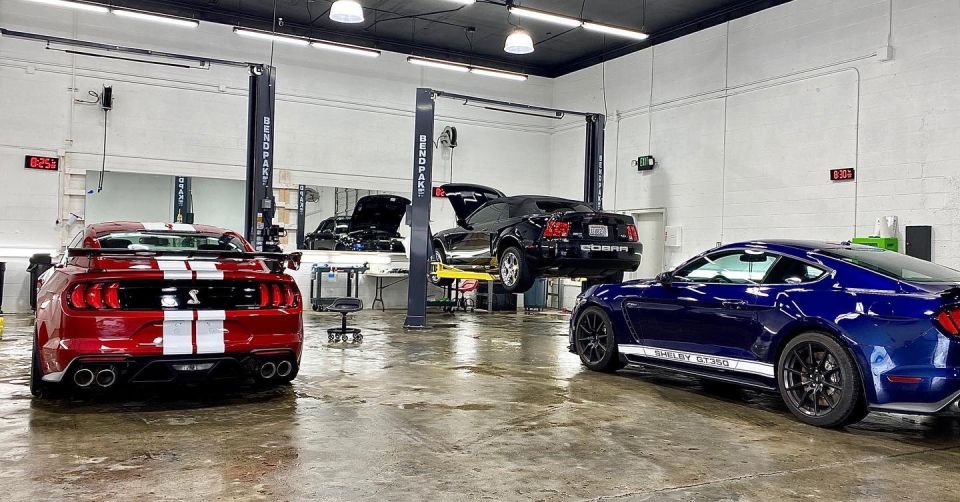 Red, blue, and black Ford Mustang Shelby models in a garage with car lifts.