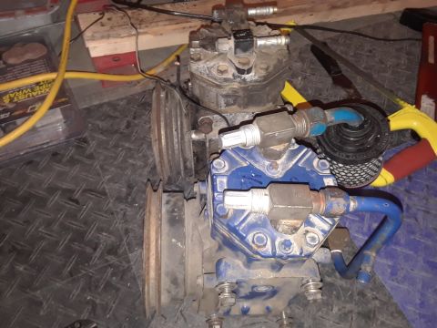 1985 Ford Bronco - A close-up view of a two-stage air compressor with blue and black components, featuring metal pulleys and various hoses and fittings. The c…