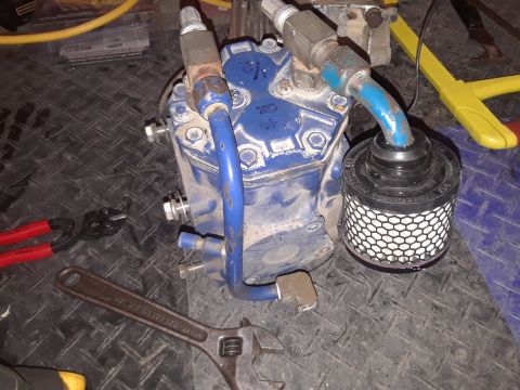 1985 Ford Bronco - A blue industrial compressor with various fittings and a black filter is shown on a black diamond plate surface. Tools including red-handle…
