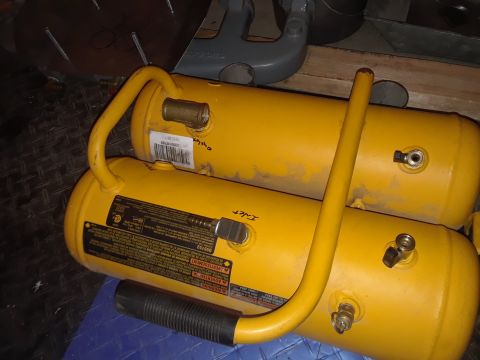 1985 Ford Bronco - Two yellow air compressor tanks are stacked on top of each other. The top tank has a brass fitting and a barcode label. The bottom tank has…