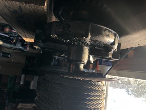 1980 Ford Bronco - This is a close-up, low-angle shot of a winch drum heavily laden with cable, mounted beneath a wooden beam. A metal housing with visible gr…