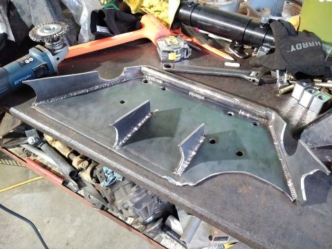 1985 Toyota Hilux - A custom metal component, likely for automotive use, sits on a workbench surrounded by tools and workshop supplies.