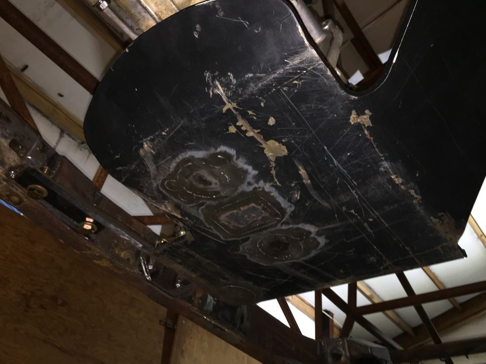 underside of a black vehicle part with scuffs and some patched areas, mounted on metal supports