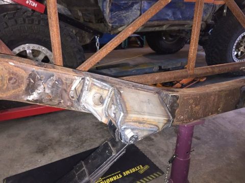 1985 Toyota Hilux - Close-up of a heavily modified vehicle chassis, extensive welding and large off-road tires, suggesting custom fabrication.