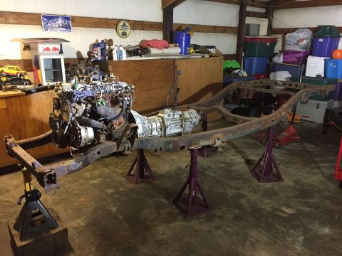 1985 Toyota Hilux - A rusty vehicle frame with an engine and transmission assembly is supported by jack stands in a garage. Various storage bins and automotive…