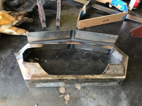 1992 Jeep Wrangler - Hand-fabricated bare steel patch panel with welded bends sitting on a workbench beside welding gloves and tools.
