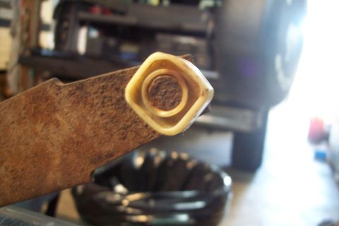 1995 Ford Bronco - Close-up of a rusty metal bracket and its plastic bushing, with a vehicle in the background.