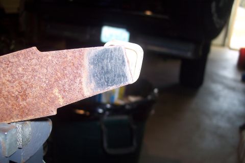 1995 Ford Bronco - A close-up view of a rusty metal component supported by a jack stand, with a vehicle partially visible in the background.