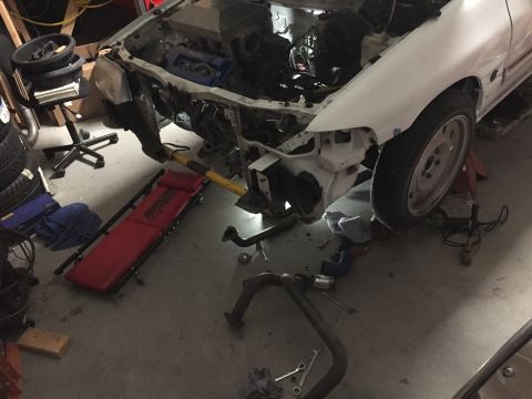 1993 Mercury Tracer - The front end of a white car is disassembled, revealing the engine and surrounding components, with exhaust pipes and tools scattered on th…