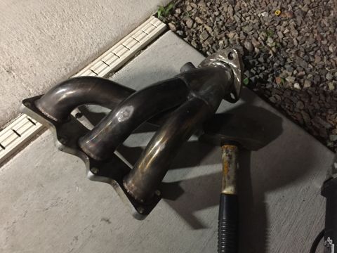 1993 Mercury Tracer - An exhaust manifold is shown resting on a concrete surface next to gravel.