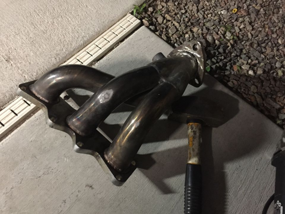 Exhaust manifold with four pipes and a flange, resting on concrete
