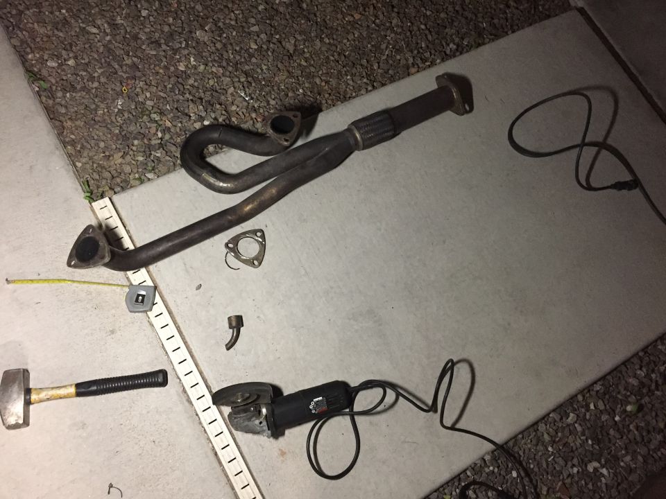 Exhaust manifold, angle grinder, hammer, and tape measure on concrete