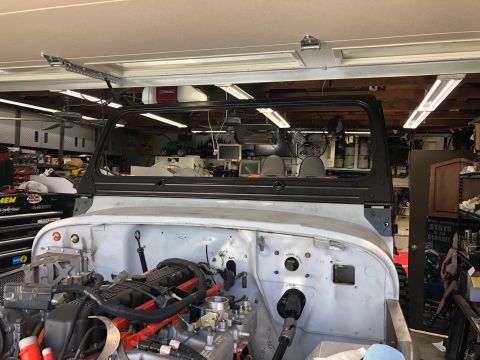 1992 Jeep Wrangler - A Jeep Wrangler body is undergoing work in a garage, with its engine compartment visible.