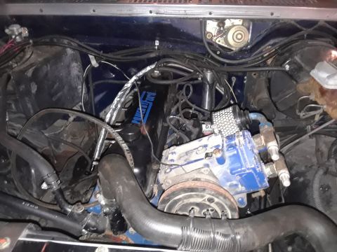 1985 Ford Bronco - Engine bay view showing the engine block, hoses, and wiring. Some text is visible on the engine cover.