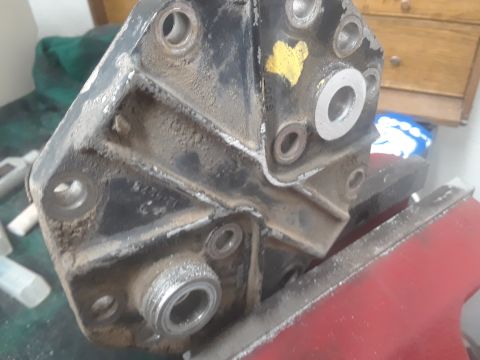 1985 Ford Bronco - A close-up view of a dusty, black metal automotive component with multiple mounting points and threaded connections.