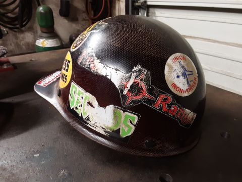 1985 Toyota Hilux - A hard hat covered in stickers sits on a workbench, with a gas cylinder in the background.
