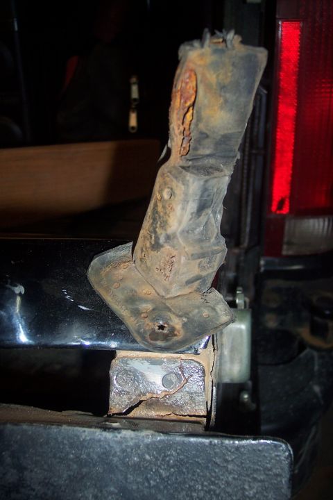 1995 Ford Bronco - Close-up of a heavily rusted bumper bracket on the rear of a vehicle, with a red tail light in the background.