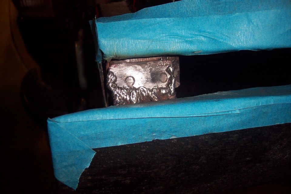 Close-up of a metal bracket with visible welds, covered in blue masking tape