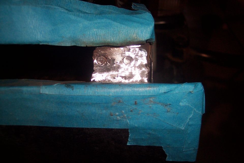 Close-up of a metal bracket with two circular indentations, covered in blue masking tape
