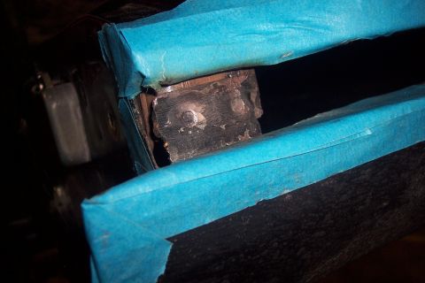 1995 Ford Bronco - Close-up of a metal bracket with bolts, partially covered in blue tape, showing signs of wear and repair.