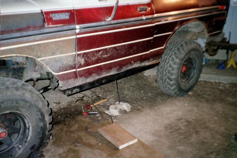 1979 Ford Bronco - Driver-side rocker view of a two-tone maroon and white Ford Bronco in a garage, with a black tube rock slider/side bar welded beneath the c…