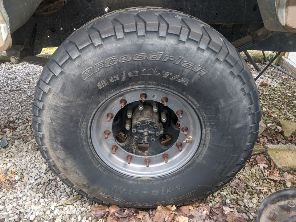 BFGoodrich Baja T/A tire on a silver rim with multiple lug nuts, viewed from the side