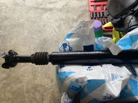 1994 Ford Bronco - Driveshaft with U-joint and rubber boot, resting on bags with tools in background.