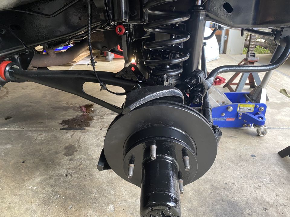 Front suspension and brake assembly of a black Ford Bronco, showing new parts and a hydraulic jack.