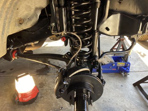 1994 Ford Bronco - A close-up, low-angle view of the front suspension and brake assembly of a vehicle, likely a truck or SUV, undergoing maintenance. The susp…