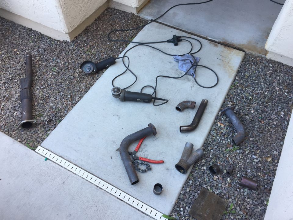 Exhaust pipe parts and angle grinders on a concrete slab.