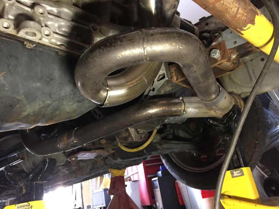 Underside of a vehicle showing custom exhaust pipes and engine components supported by jack stands.