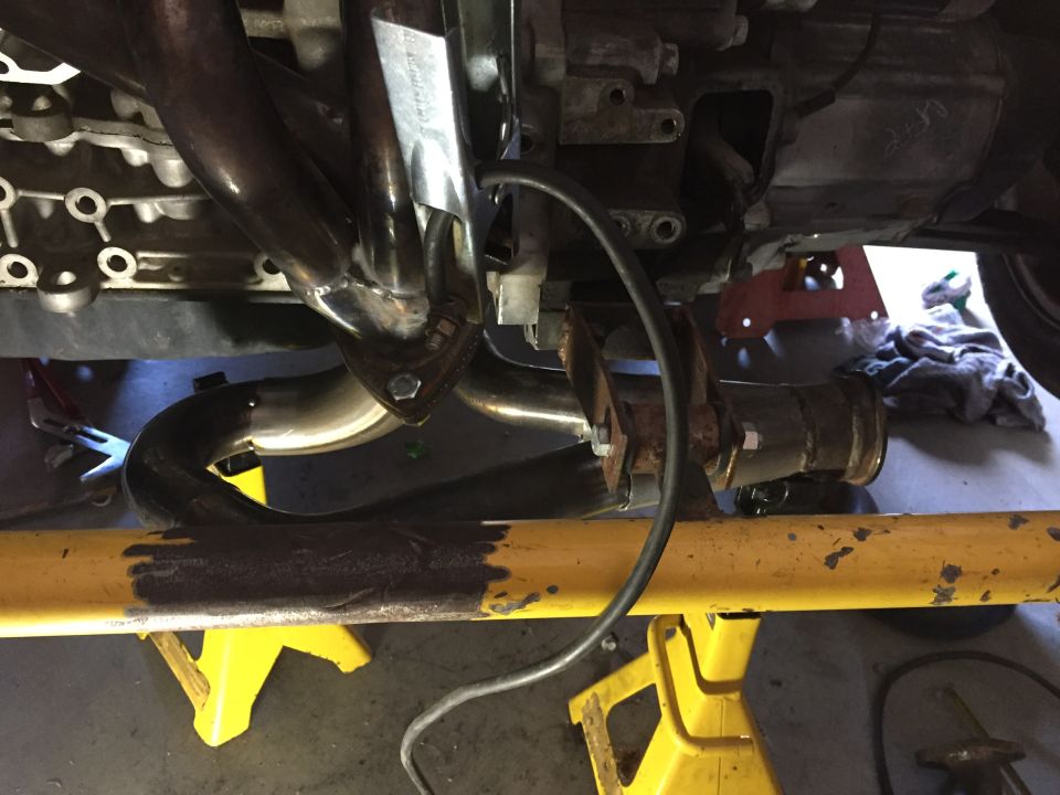 Close-up of exhaust system and engine components on a vehicle supported by jack stands.