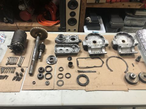 1980 Ford Bronco - A collection of disassembled engine or transmission parts, including gears, casings, bolts, and bearings, are laid out on a cardboard-cover…