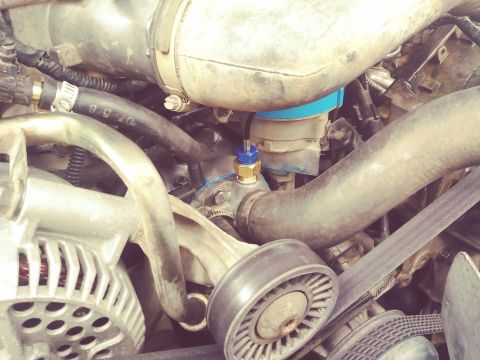 1996 Ford Bronco - A close-up view of the engine bay of a 1996 Ford Bronco, showing various hoses, belts, and an alternator. A blue and gold sensor is visible…