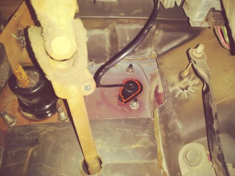 1996 Ford Bronco - A close-up view of the steering column and firewall area of a vehicle, showing a black rubber grommet with an orange seal around a wire pas…